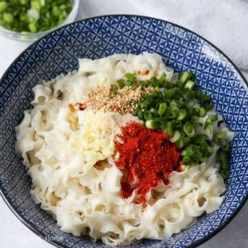 In the center, on top of the noodles, add regular soy sauce, dark soy sauce, Chinese black vinegar, garlic, chicken bouillon powder, white granulated sugar, green onions, red chili flakes, sesame seeds and set aside.