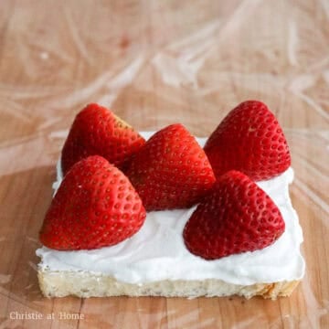Lay a large sheet of plastic wrap on a cutting board and place one slice of bread on top. Spread a thin, even layer of whipped cream over the surface. Arrange the strawberries in an "X" pattern, all facing the same direction. Take note of their orientation for slicing later.