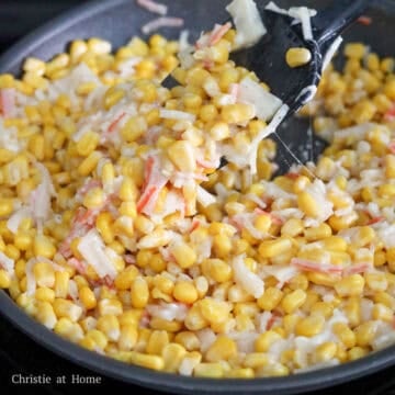 Shredded mozzarella cheese being mixed into the hot corn mixture in a pan.