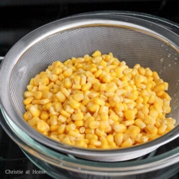 Straining canned corn through a fine mesh sieve to remove excess liquid.