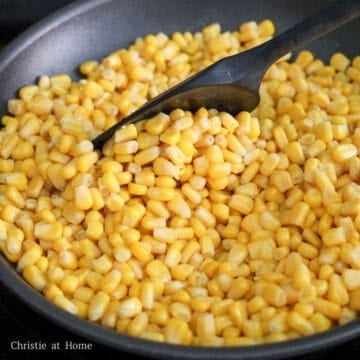 Corn cooking in melted butter in a non-stick pan on the stovetop.