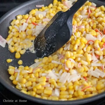 Corn and imitation crab mixture being stirred in a skillet with mayonnaise and seasonings as it cooks.