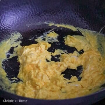 Eggs being poured into a hot wok with oil and quickly stir-fried until just set but still soft.