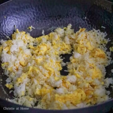 Cooked rice being added to the wok and broken apart with a spatula to remove clumps.
