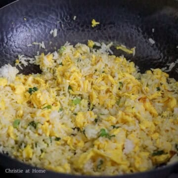 Green onions sizzling in oil on one side of the pan while rice and eggs are pushed aside and mixed back together.