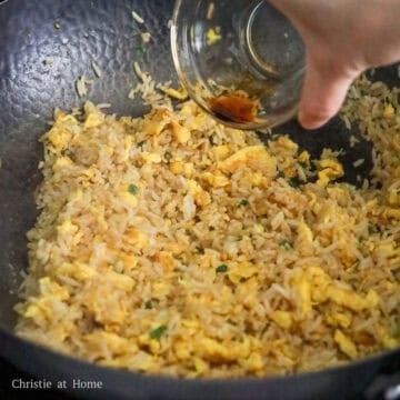 Soy sauce and sesame oil being drizzled around the edge of the hot pan as fried rice is tossed until evenly coated and lightly browned.