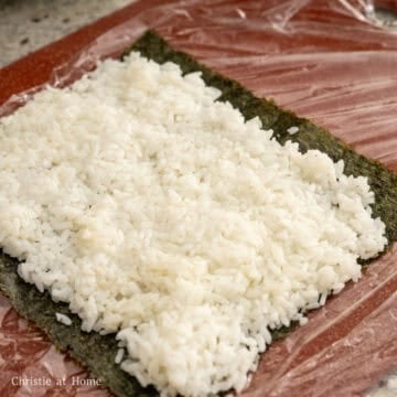 On a bamboo mat or sushi mat (or plastic wrap set on a cutting board), place your a sheet of nori horizontally rough side up, shiny side down. Evenly spread 1 cup of seasoned rice leaving a ½ inch border at the ends.