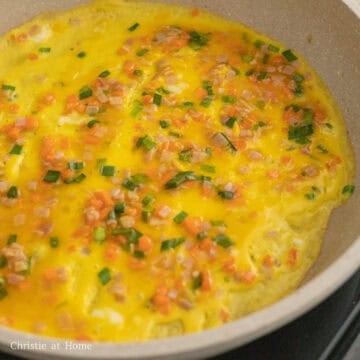 Then in a large nonstick pan set over medium-low heat, lightly grease it with vegetable oil using a clean paper towel. Pour a very thin layer of the egg mixture and quickly spread it into an egg pancake by rotating the pan and using your chopsticks to spread the chopped ingredients evenly. The egg pancake should reach the edge of the pan.