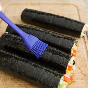 Then place kimbap on a cutting board and brush ¼ teaspoon sesame oil all over each kimbap.