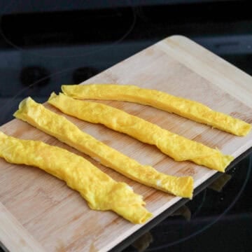Remove the egg roll from the pan and slice into two equal strips. Repeat process for remaining egg mixture. You should have 4 long strips of cooked egg.