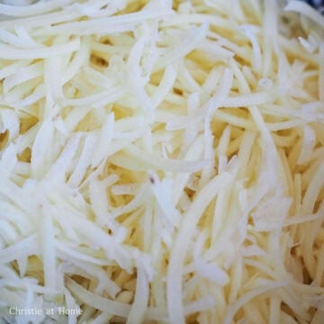 First grate your peeled potatoes with a box grater or a food processor on the smaller setting. Transfer grated potatoes to a colander.