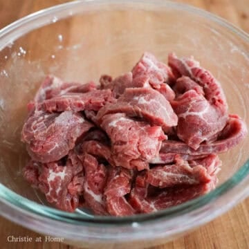 Sliced beef being tossed with marinade ingredients in a bowl.