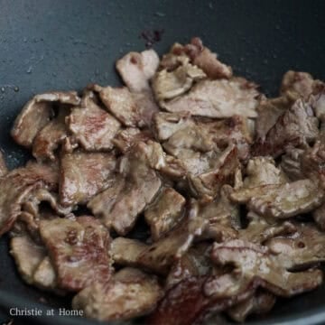 Beef strips being seared in a pan until slightly browned on the edges.