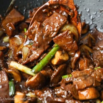 Cooked beef stir-fry with mushrooms, onions, and green onions in a glossy sauce, ready to serve.